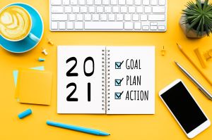 yellow desk with a mug of coffee, pencils, keyboard, and smartphone visible as well as an open planner with the word "2021, goal, plan, and action" written in it