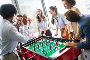 group of office colleagues laugh while playing foosball 