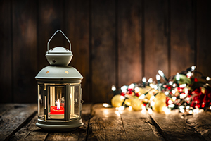 lantern with a red candle burning sits next to a pile of illuminated electric Christmas lights 