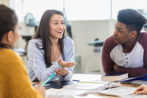 female students smiling and gesturing with her hand while studying with other students 