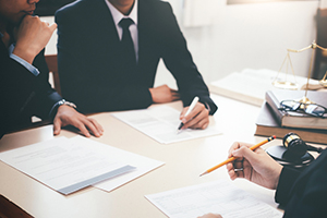 three business people dressed in black suits sit around a table with scattered papers