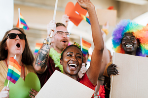 diverse group of people smile and celebrate while displaying rainbow pride flags