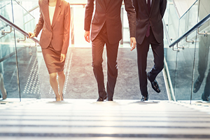 three business people dressed in suits walk up a staircase together 