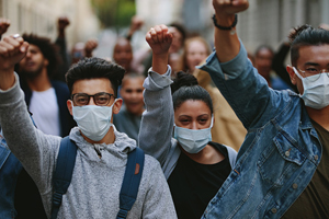 mass of people wearing face masks as some of them raise their fists in the air while they protest