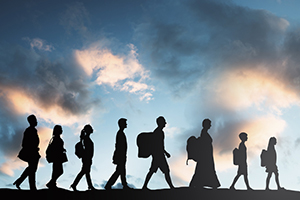 group of silhouettes against a cloudy background walk after each other in a line 