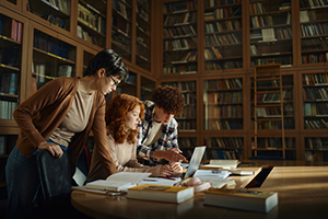 Three individuals working on a project in a library.