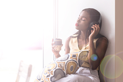 woman sitting serenely near window while wearing headphones and drinking tea