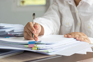 person in white shirt writes on a stack of paper with a pen 