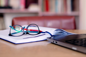 glasses and pen on open notebook in front of laptop