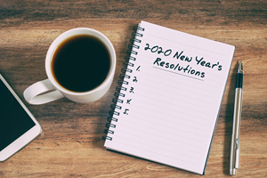 notebook with "2020 New YEar's Resolutions" written on it with 5 numbers, next to a cup of coffee and a pen