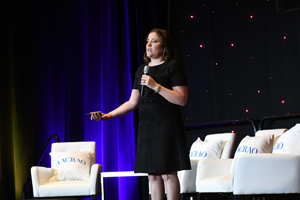 Sara Goldrick-Rab speaking from a stage with white cushioned chairs behind her