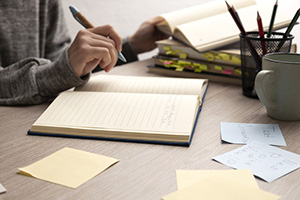 Individual writing in a notebook at a desk.