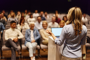 Photograph of an individual speaking in front of an audience.