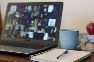 laptop resting on a desk with a blue mug, apple, and notepad and pen visible next to the laptop