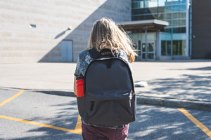 young student wearing a backpack walks towards a building
