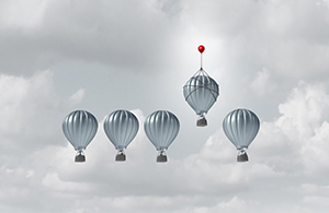 group of silver got air balloons floating in a cloudy sky with one floating above the rest 