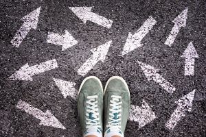 green canvas sneakers standing on asphalt with multiple white arrows painted in jumbled directions 