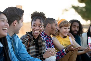 diverse group of young adults smiling and chatting while seated in a line together