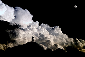 Individual standing on a mountain facing a large cloud bank.