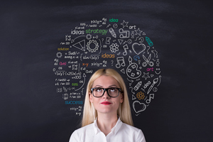 woman standing against blackboard with facts and figures written on it to illustrate genius