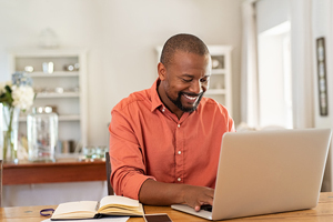 male in a salmon colored dress shirt smiles while working on his laptop
