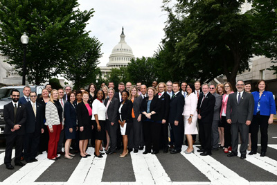 Large group of AACRAO members dressed in formal business attire as they stand in a cross walk with the U.S. Capitol visible in the background.