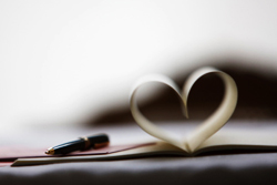 Photo of a pen on top a notepad whose pages are folded such that they form a heart shape.
