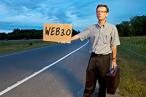 Male hitchhiker in business attire holding a cardboard sign by the side of the road that says "Web3.0".