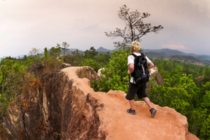 Figure wearing a backpack as they walk along a narrow path with sheer drops on either side.