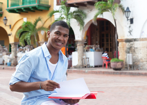 Male student of color smiling at the camera as he flips through a notebook.