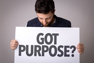 Male holding a white sign with the words "Got Purpose?" written on it in bold black lettering.