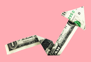 Salmon colored background with an upward trending arrow made from a folded dollar bill.