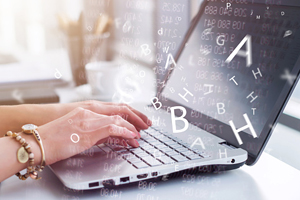 Pair of hands typing on a laptop as various letters float away from the keyboard.