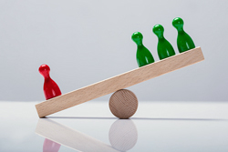 Simple lever and fulcrum made of wood with three green board game pieces on the high side of the lever and one red piece on the low side.