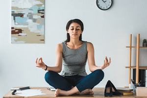 Female dressed in active wear as she sits with her eyes closed in a meditative pose.