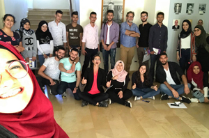 Group photo with some people standing while others sit in front on a wooden floor.