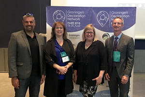 Four business professionals smiling in front of a step & repeat that says "Groningen Declaration Network."