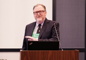 Male speaking from behind a wooden podium.