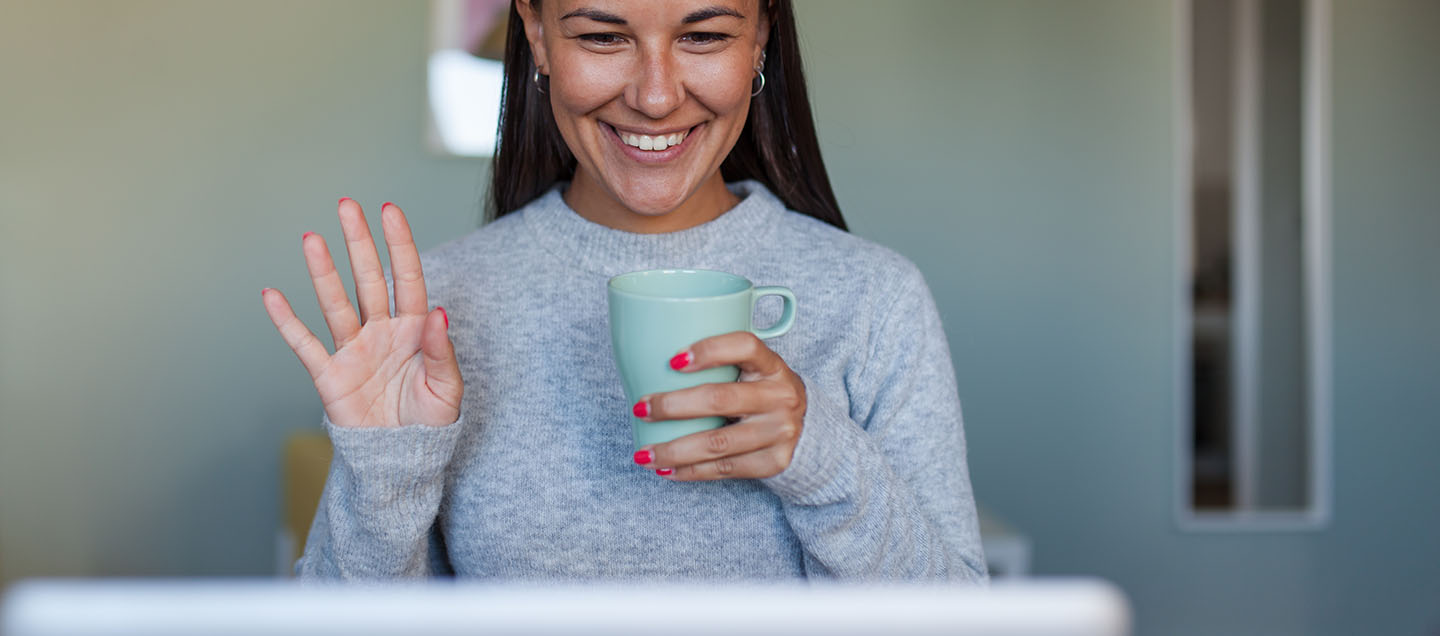 Female waving at her computer presumably because she's on a video conference call. 