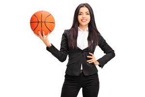 female in a business suit holds up a basketball ball with one hand while the other hand is on her hip