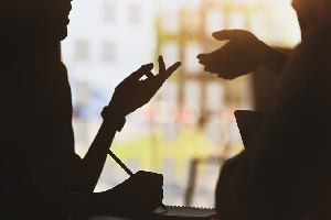 Two silhouettes conversing while one takes notes.