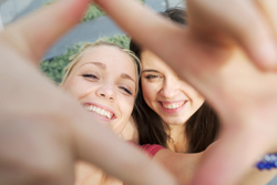 Two females smiling together as one of them frames the picture with her hands.