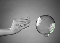 Grey-scale photo of a hand holding out a needle to an iridescent soap bubble.