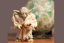 Miniature figurine of the Jedi master, Yoda, in front of a small ball with swirled bits of blue and beige on it.