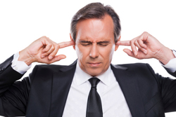 Male wearing a business suit while he plugs his ears with his fingers.
