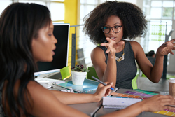 Two females of color conversing over an office desk. 