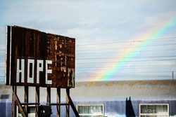 Rusted road-side billboard with the word "hope" written on it in white and a rainbow in the background.