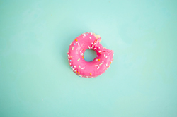 Solid sea green background with a pink donut with a single bite missing in the center of the image.