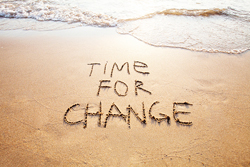 The phrase "time for change" written in the sand as waves threaten to wash it away.