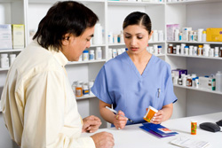 Female pharmacist speaking with a male in a collared dress shirt.